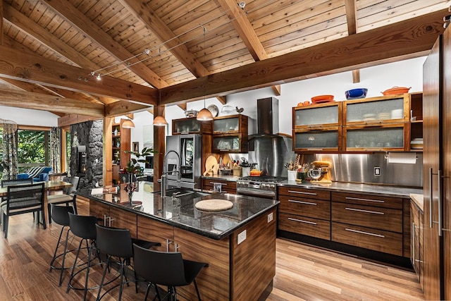 kitchen featuring a large island with sink, light wood-type flooring, a breakfast bar area, and wall chimney range hood