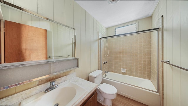 full bathroom featuring tiled shower / bath, vanity, wooden walls, and toilet