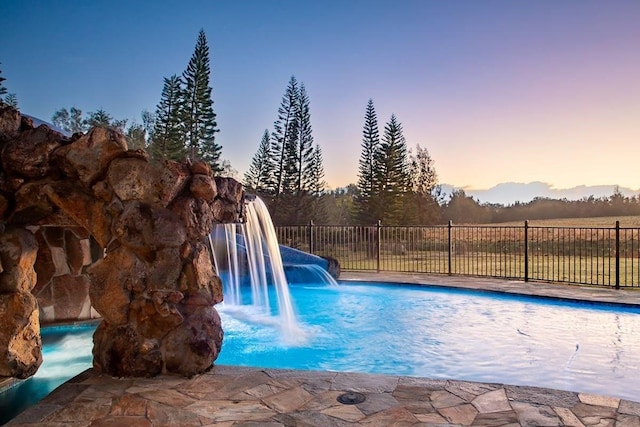 pool at dusk featuring pool water feature