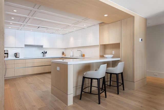 kitchen with kitchen peninsula, a kitchen breakfast bar, tasteful backsplash, light hardwood / wood-style flooring, and white cabinetry