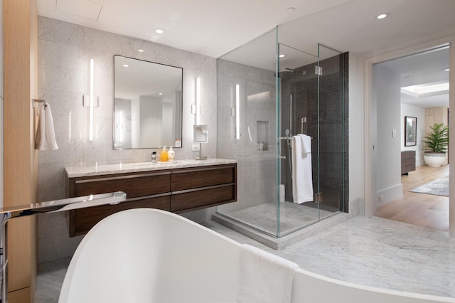 bathroom with shower with separate bathtub, vanity, hardwood / wood-style flooring, and tile walls