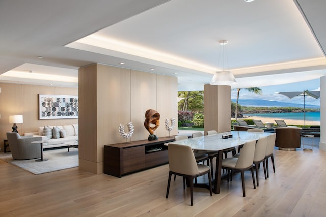 dining area featuring a tray ceiling, a water view, and light wood-type flooring