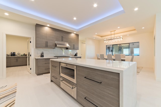 kitchen with light stone counters, backsplash, pendant lighting, a tray ceiling, and a kitchen island