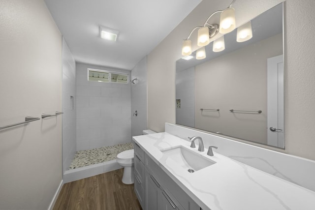 bathroom featuring tiled shower, vanity, wood-type flooring, and toilet