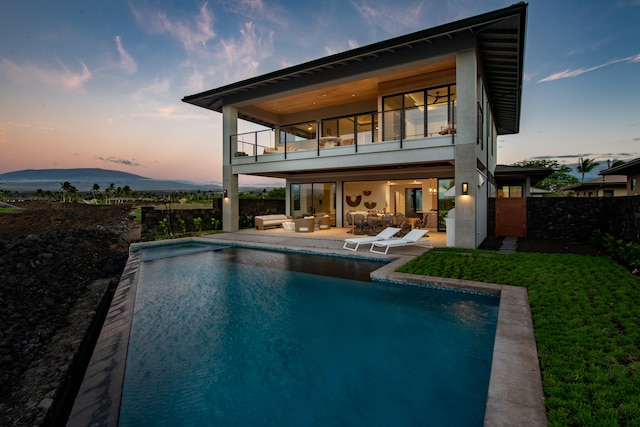 back house at dusk featuring an outdoor hangout area, a balcony, a fenced in pool, and a patio