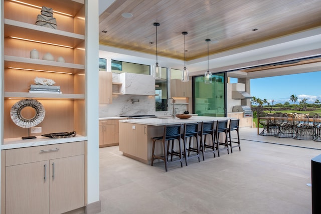 kitchen featuring hanging light fixtures, wood ceiling, a kitchen island with sink, and a breakfast bar area