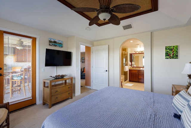 bedroom with ceiling fan, light colored carpet, ensuite bathroom, and a tray ceiling