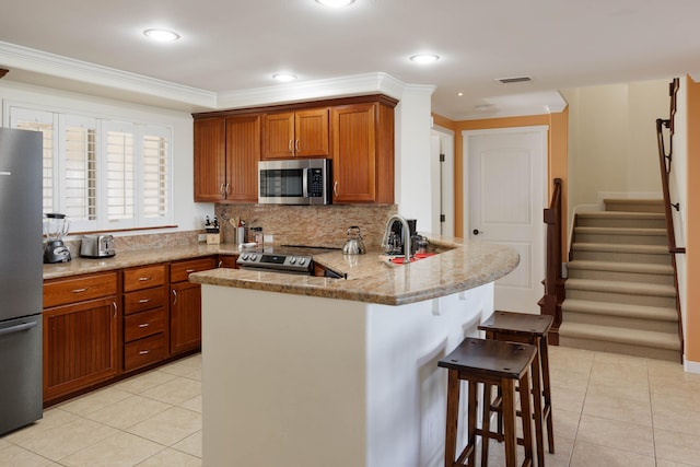 kitchen featuring kitchen peninsula, light stone countertops, tasteful backsplash, a breakfast bar, and stainless steel appliances