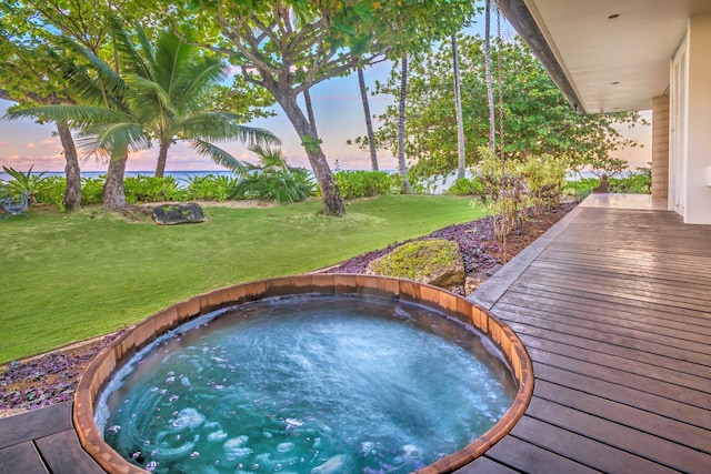 pool at dusk featuring a jacuzzi and a yard