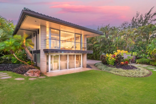 back house at dusk featuring a yard and a balcony