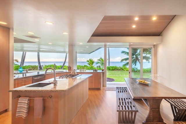 kitchen featuring a water view, sink, light wood-type flooring, an island with sink, and light brown cabinetry