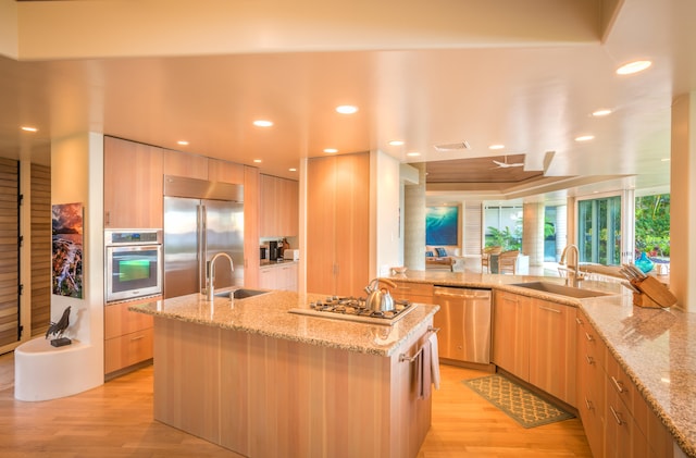 kitchen featuring light stone counters, a center island with sink, stainless steel appliances, and sink