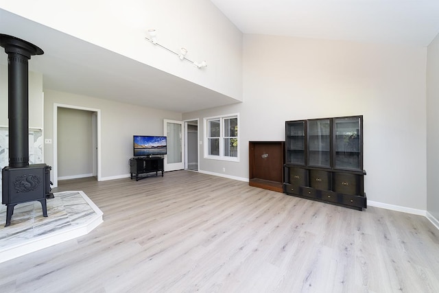 living room featuring high vaulted ceiling, light hardwood / wood-style floors, and a wood stove