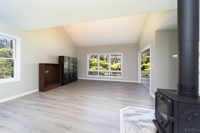 living room with plenty of natural light, light hardwood / wood-style floors, vaulted ceiling, and a wood stove