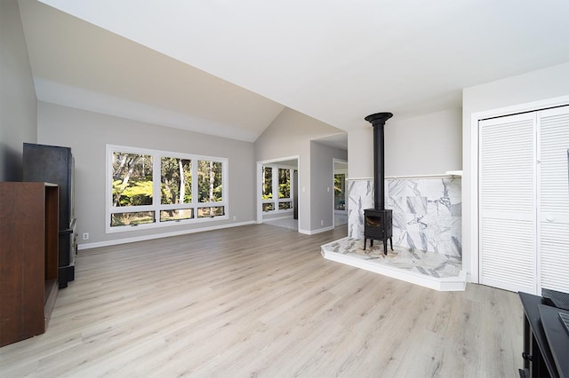 unfurnished living room featuring lofted ceiling, a wood stove, and light hardwood / wood-style flooring