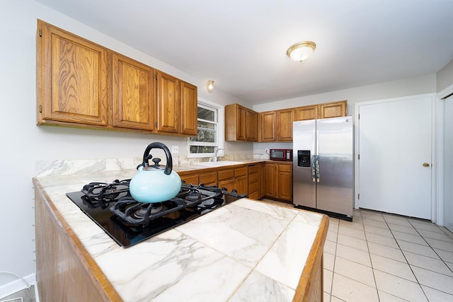 kitchen featuring tile counters, stainless steel fridge, sink, and black gas cooktop