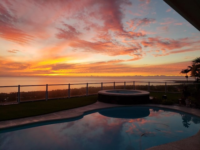 pool at dusk with an in ground hot tub and a water view