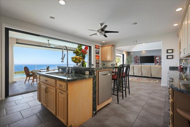 kitchen with light brown cabinets, a kitchen island with sink, a water view, sink, and stainless steel dishwasher