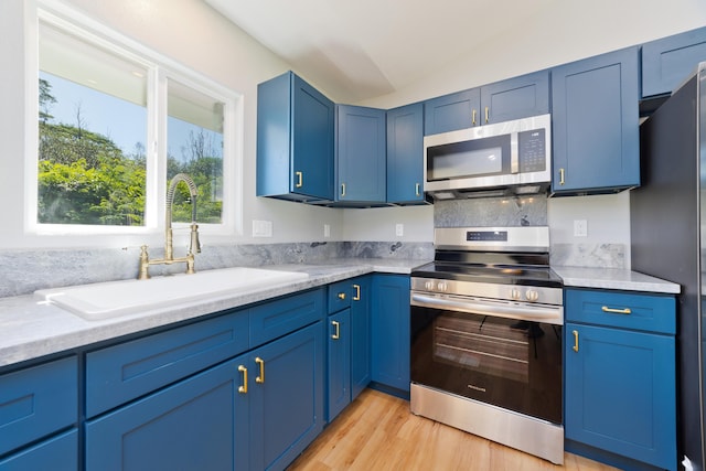 kitchen with blue cabinetry, sink, light hardwood / wood-style flooring, lofted ceiling, and appliances with stainless steel finishes