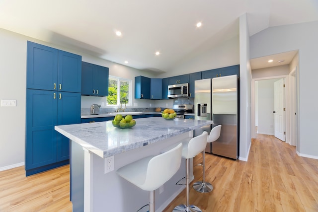 kitchen featuring a center island, vaulted ceiling, a breakfast bar, appliances with stainless steel finishes, and light wood-type flooring