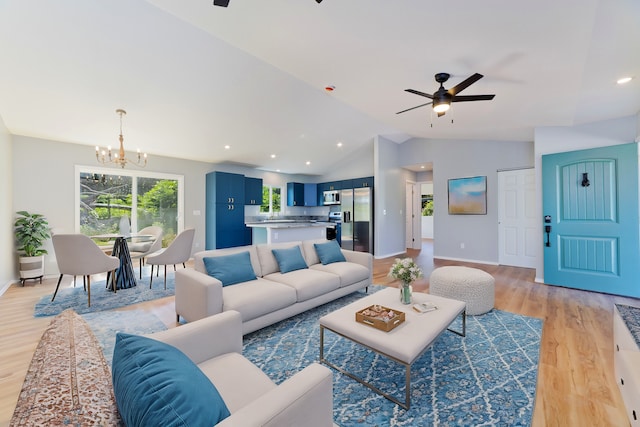 living room featuring ceiling fan with notable chandelier, light wood-type flooring, and vaulted ceiling