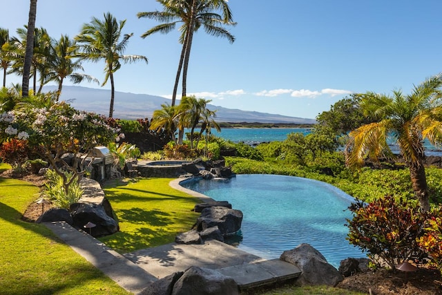 view of swimming pool featuring an in ground hot tub, a water and mountain view, and a lawn