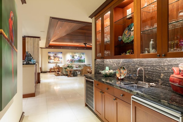 kitchen with sink, ceiling fan, decorative backsplash, dark stone countertops, and beverage cooler