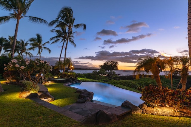 pool at dusk featuring a lawn and a water view