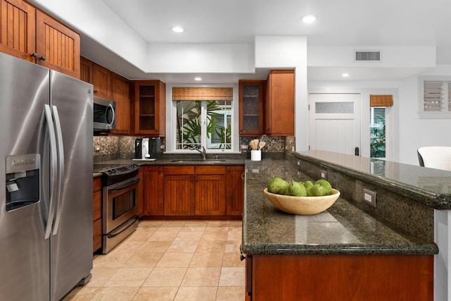 kitchen with sink, dark stone countertops, tasteful backsplash, kitchen peninsula, and stainless steel appliances