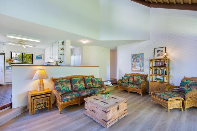 living room with wooden walls, ceiling fan, light hardwood / wood-style floors, and a high ceiling