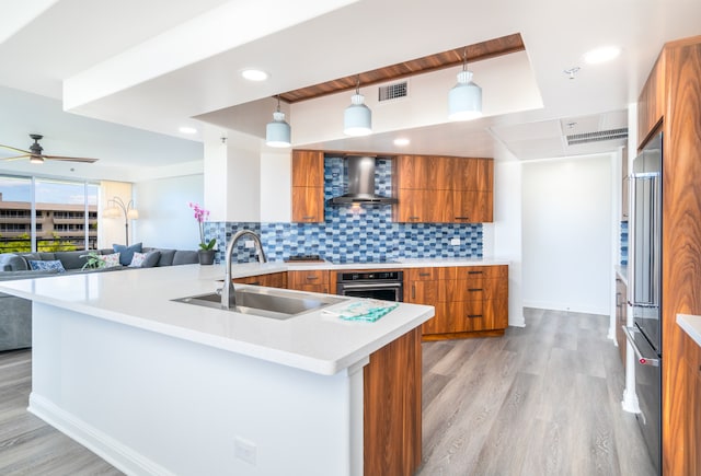 kitchen featuring stainless steel oven, hanging light fixtures, wall chimney range hood, tasteful backsplash, and light wood-type flooring