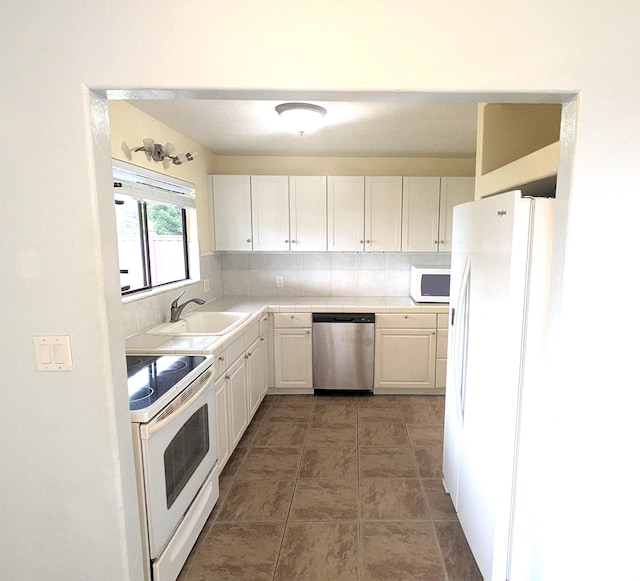 kitchen featuring sink, tasteful backsplash, dark tile patterned floors, white appliances, and white cabinets