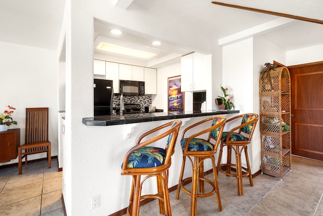 kitchen featuring light tile patterned floors, tasteful backsplash, a raised ceiling, white cabinets, and black appliances