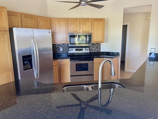 kitchen featuring ceiling fan, sink, stainless steel appliances, backsplash, and dark stone counters