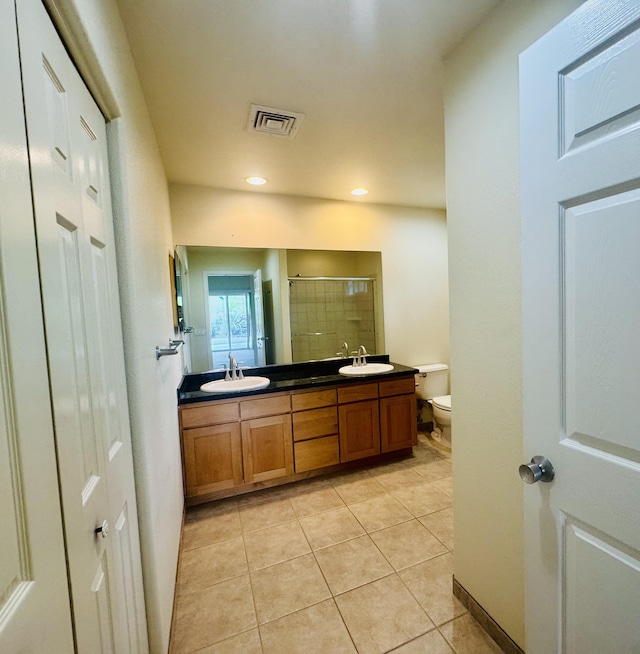 bathroom featuring toilet, tile patterned flooring, vanity, and tiled shower