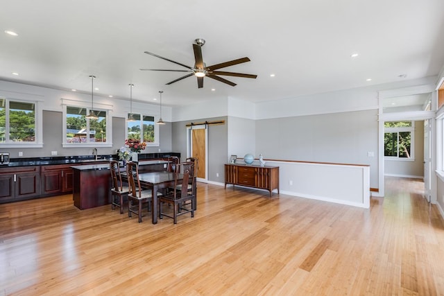 dining room with a barn door, light hardwood / wood-style floors, ceiling fan, and a healthy amount of sunlight