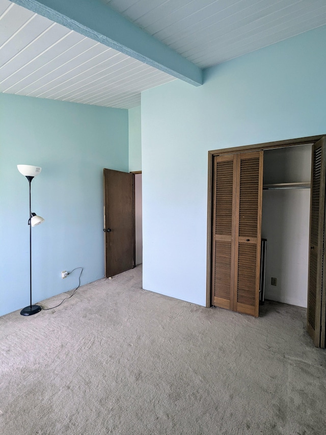 unfurnished bedroom with a closet, carpet flooring, and beamed ceiling