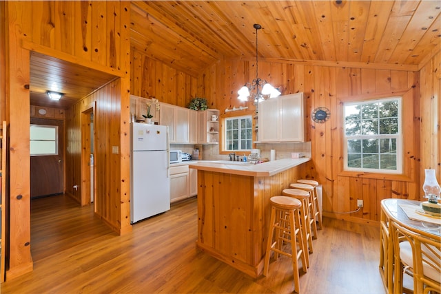 kitchen featuring lofted ceiling, white appliances, decorative light fixtures, kitchen peninsula, and a chandelier