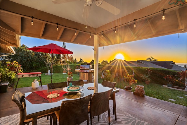 patio terrace at dusk featuring a lawn, ceiling fan, and grilling area