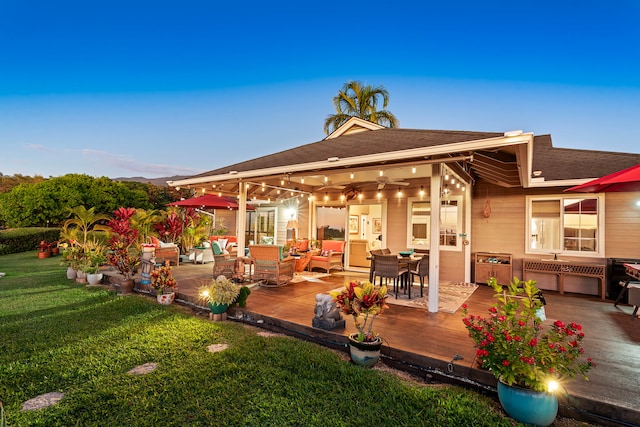 back house at dusk with a lawn, ceiling fan, and an outdoor hangout area