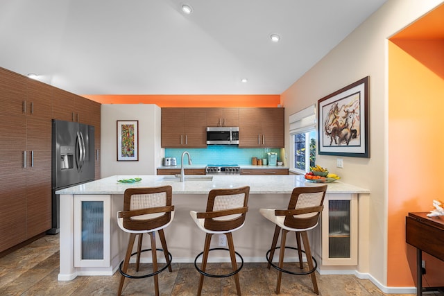 kitchen with decorative backsplash, appliances with stainless steel finishes, a kitchen bar, and sink