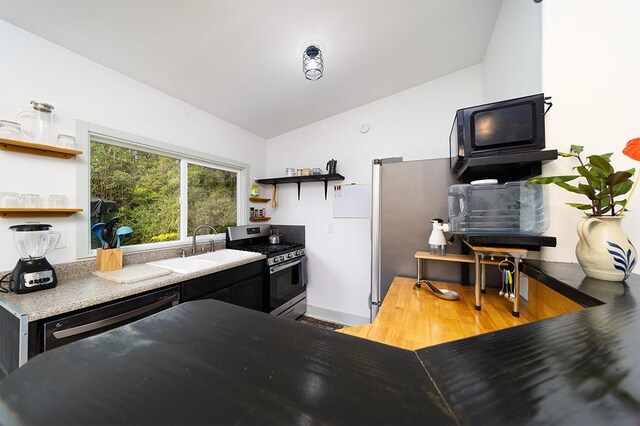 kitchen featuring sink, light wood-type flooring, vaulted ceiling, and appliances with stainless steel finishes