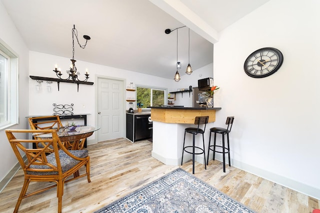 kitchen with lofted ceiling with beams, a notable chandelier, kitchen peninsula, a kitchen bar, and light wood-type flooring