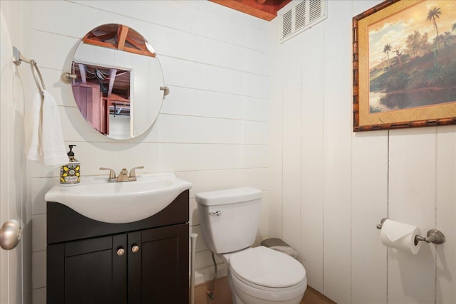 bathroom with vanity, wood walls, and toilet