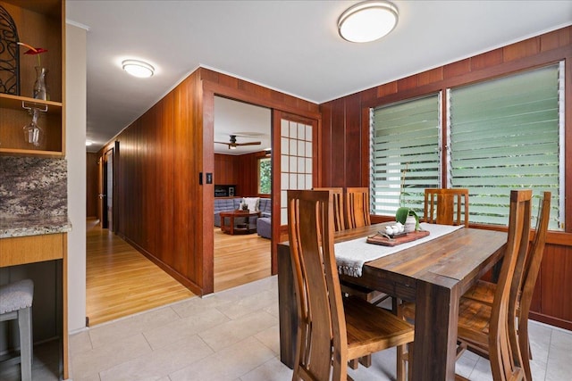 dining room featuring light hardwood / wood-style flooring, ceiling fan, and wooden walls