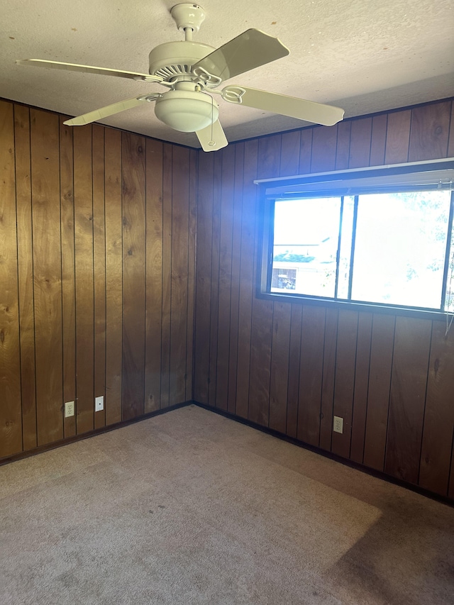 carpeted spare room featuring ceiling fan, wood walls, and a textured ceiling