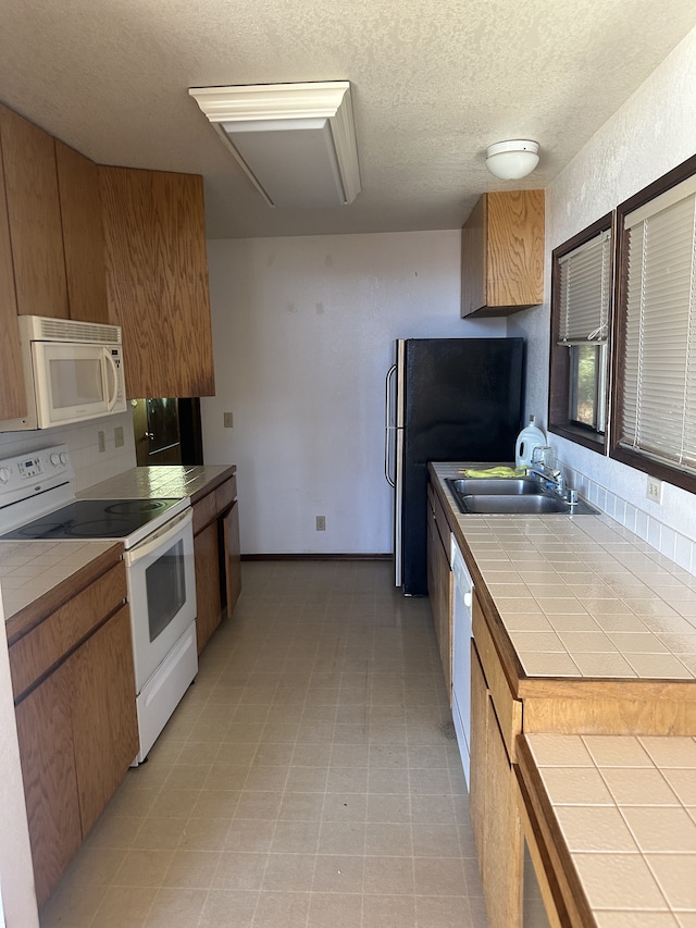 kitchen with a textured ceiling, tile countertops, sink, and white appliances