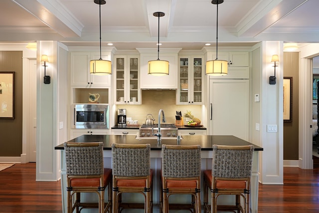 kitchen featuring a breakfast bar area, a kitchen island with sink, beamed ceiling, and built in appliances