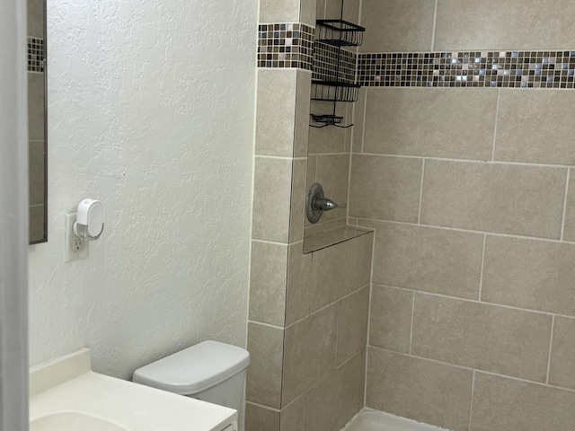 bathroom featuring toilet, vanity, and tiled shower