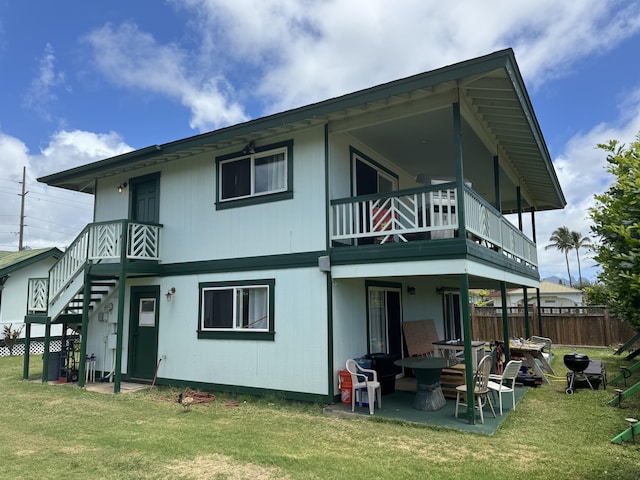 rear view of house featuring a lawn, a balcony, and a patio